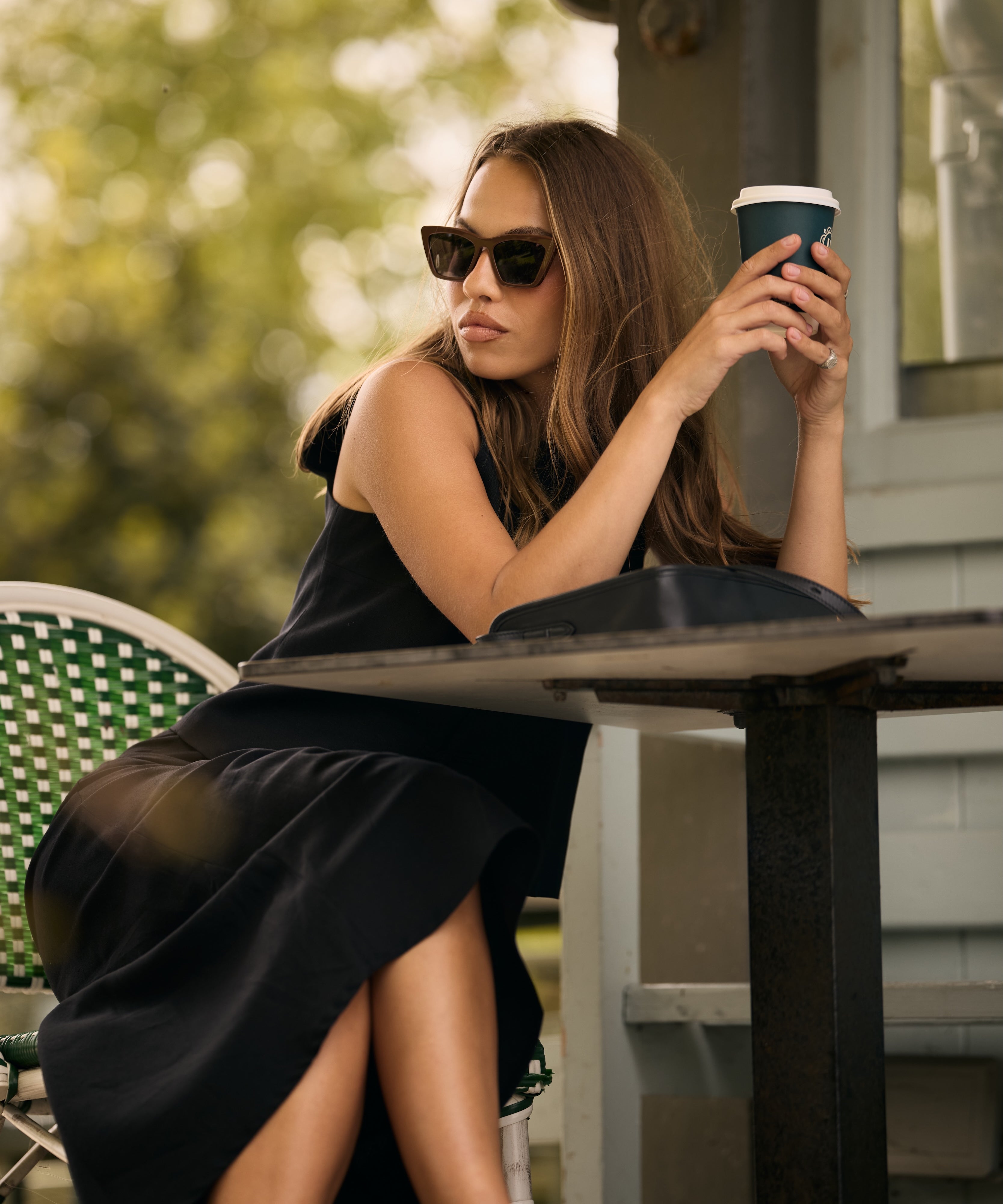 womean sitting in a cafe wearing sunglasses and drinking coffee