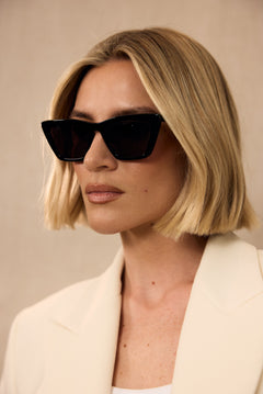 Woman wearing black sunglasses and a light-colored blazer against a neutral background