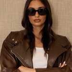 Woman wearing a brown leather jacket and sunglasses against a beige background