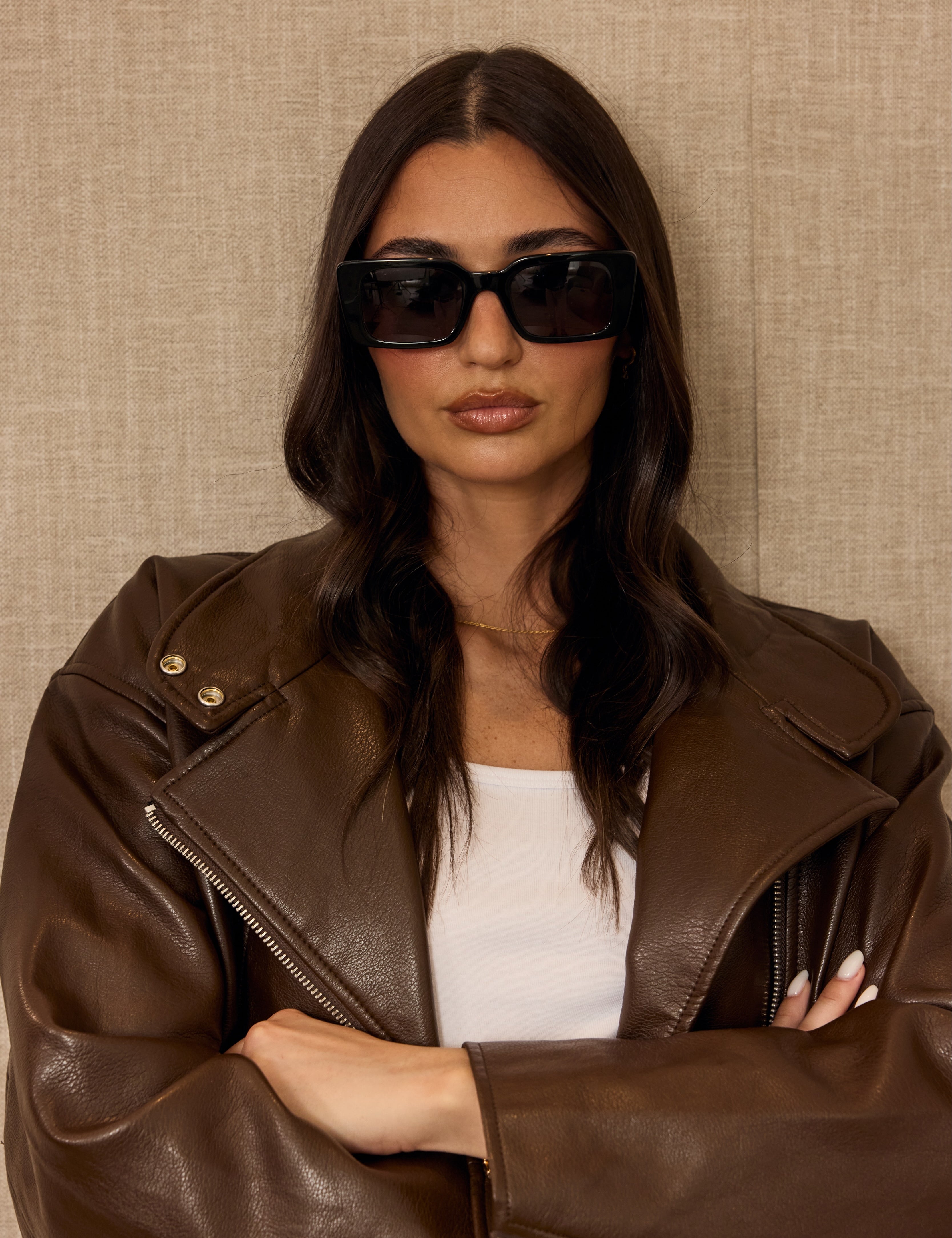 Woman wearing a brown leather jacket and sunglasses against a beige background