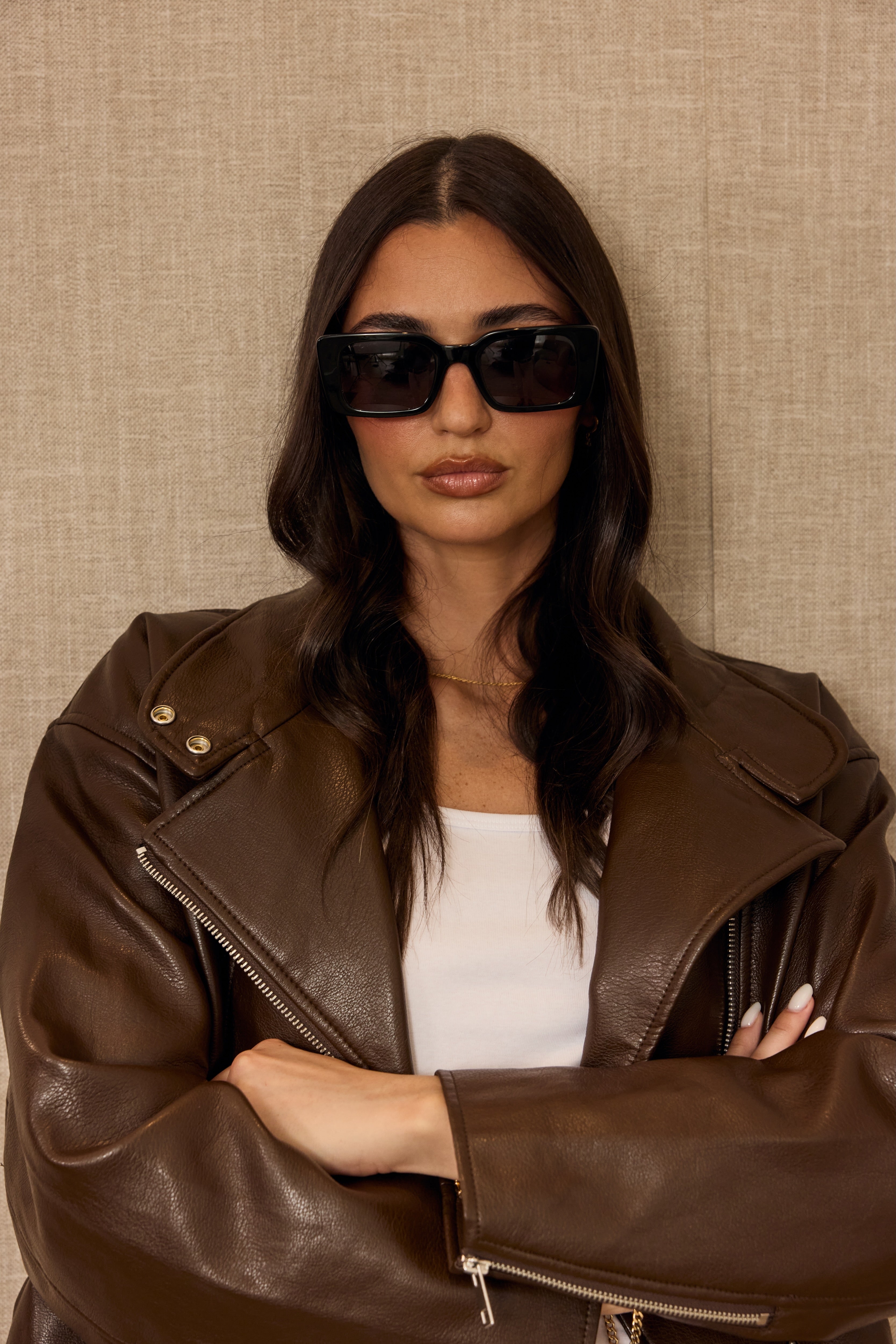 Woman wearing a brown leather jacket and sunglasses against a beige background