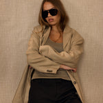 Woman wearing a beige coat and sunglasses against a beige wall