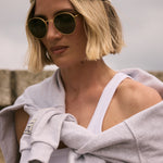 Person wearing a cap and sunglasses with a gray towel draped over their shoulder against a neutral background