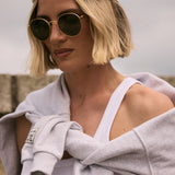Person wearing a cap and sunglasses with a gray towel draped over their shoulder against a neutral background